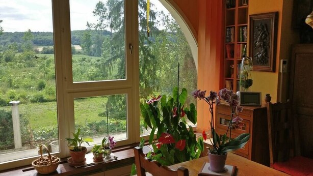 A room with a large window offering a view of a green landscape, a wooden table with chairs, and a bookshelf with various items. - A spacious vacation rental perfect for family getaways: games, nature, and tranquility (Villotte-sur-Aire)