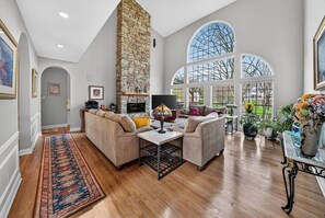 A spacious living room with a stone fireplace, large windows, and a variety of seating arrangements.