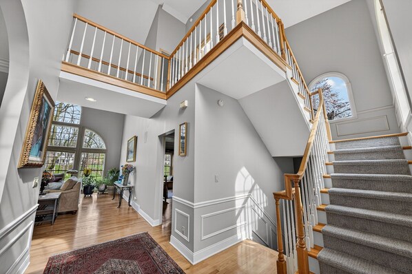 A spacious interior with a grand staircase, high ceilings, and large windows.
