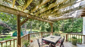 Une terrasse en bois avec une table et des chaises, entourée d’une balustrade en bois et de plantes en pot.