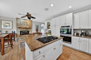 A kitchen with white cabinetry, a granite countertop, a gas stove, an oven, and a ceiling fan.