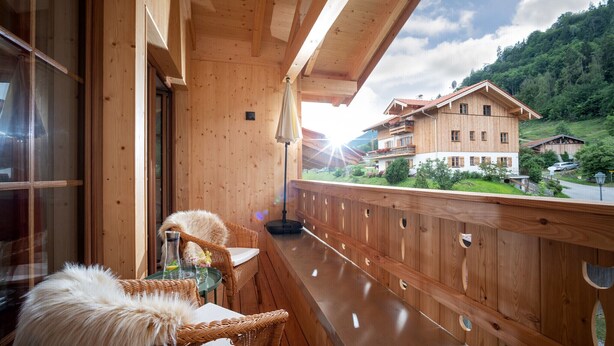 A wooden balcony with wicker furniture and a view of a mountain house. - Apartment Kranzhorn, 75sqm, balcony (Oberaudorf)