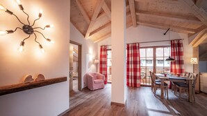 A wooden ceiling, a dining area with a table and chairs, and a pink chair in a hallway. - Apartment Kranzhorn, 75sqm, balcony (Oberaudorf)