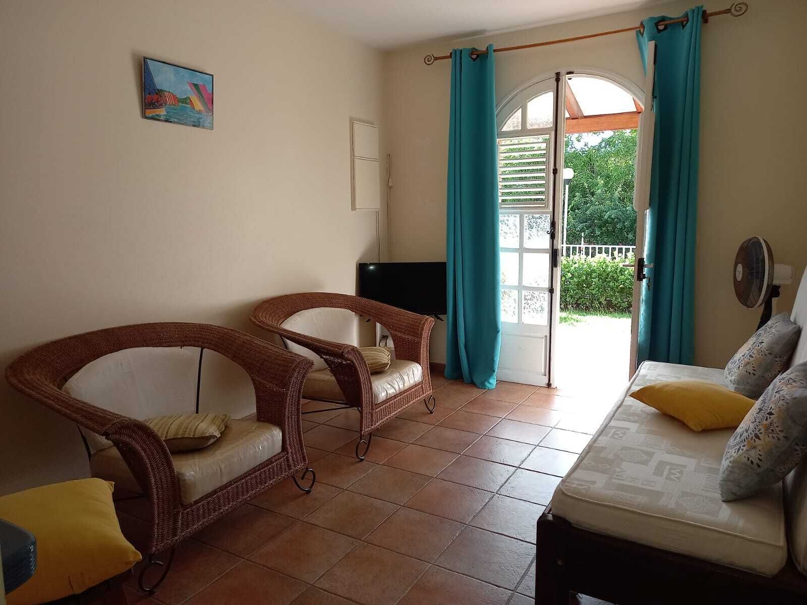 A room with two wicker chairs, a sofa, a TV, and a window with curtains.