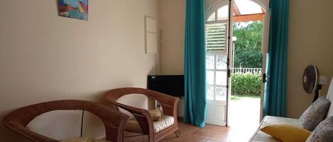 A room with two wicker chairs, a sofa, a TV, and a window with curtains.