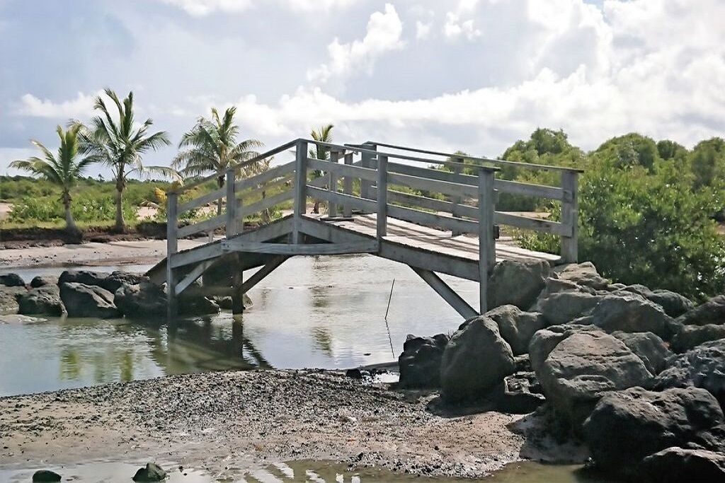 Eine Holzbrücke über ein Gewässer mit Felsen an beiden Seiten.