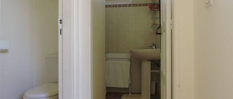 Een smalle gang die leidt naar een badkamer met toilet, wastafel en handdoekrek.