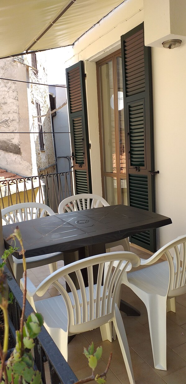 A balcony with a table and chairs, a sliding glass door, and a view of a building with stone walls.