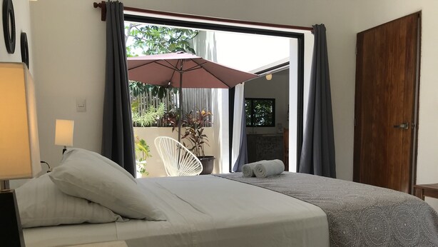 Una camera da letto con un letto, una sedia, una pianta in vaso e vista sull'esterno.