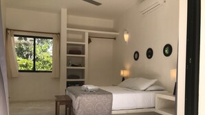 Una camera da letto con un letto, una piccola panca, una finestra con tende, uno scaffale con vestiti piegati e lampade a parete.