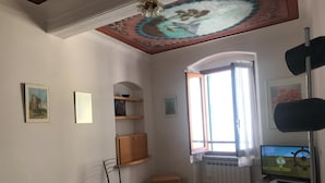 A living room with a sofa, a small table, a TV, and a window with curtains. -  Apartment in Riomaggiore / Cinque Terre (Riomaggiore)