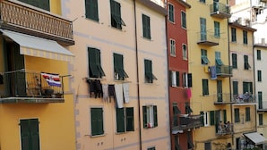 A multi-story building with balconies, a street-level shop, and a church in the background. -  Apartment in Riomaggiore / Cinque Terre (Riomaggiore)