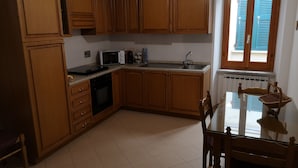 A kitchen with wooden cabinets, a microwave, a sink, and a dining table with chairs. -  Apartment in Riomaggiore / Cinque Terre (Riomaggiore)