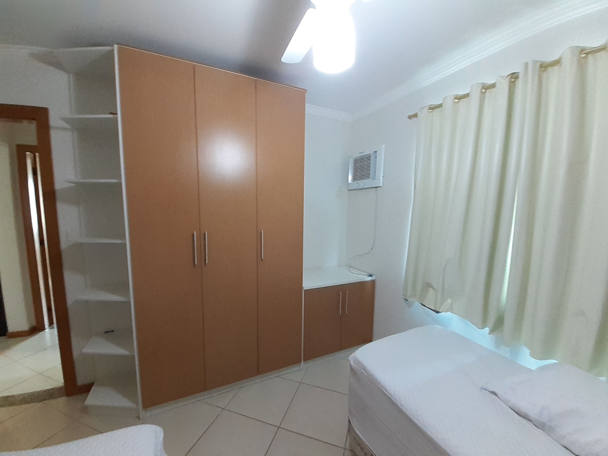 Un dormitorio con cama, armario, radiador y ventana con cortinas.