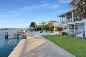 Enjoy waterfront views from the upper-level balcony of this modern property, surrounded by a well-manicured lawn and tropical plants.