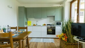 A compact kitchen with a dining area, featuring a wooden table, chairs, a microwave, a stove, and a TV.