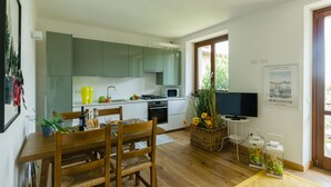A modern kitchen with green cabinets, a dining area with wooden furniture, and a TV on the wall.