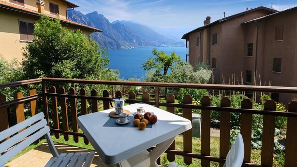 A balcony with a table set for two, overlooking a lake and mountains.