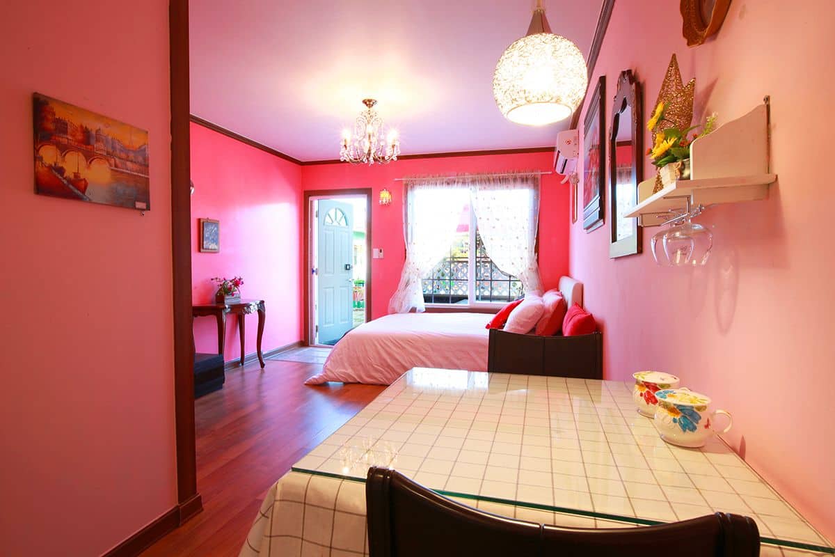 A pink-themed bedroom with a bed, a chandelier, and a dining table with teacups.