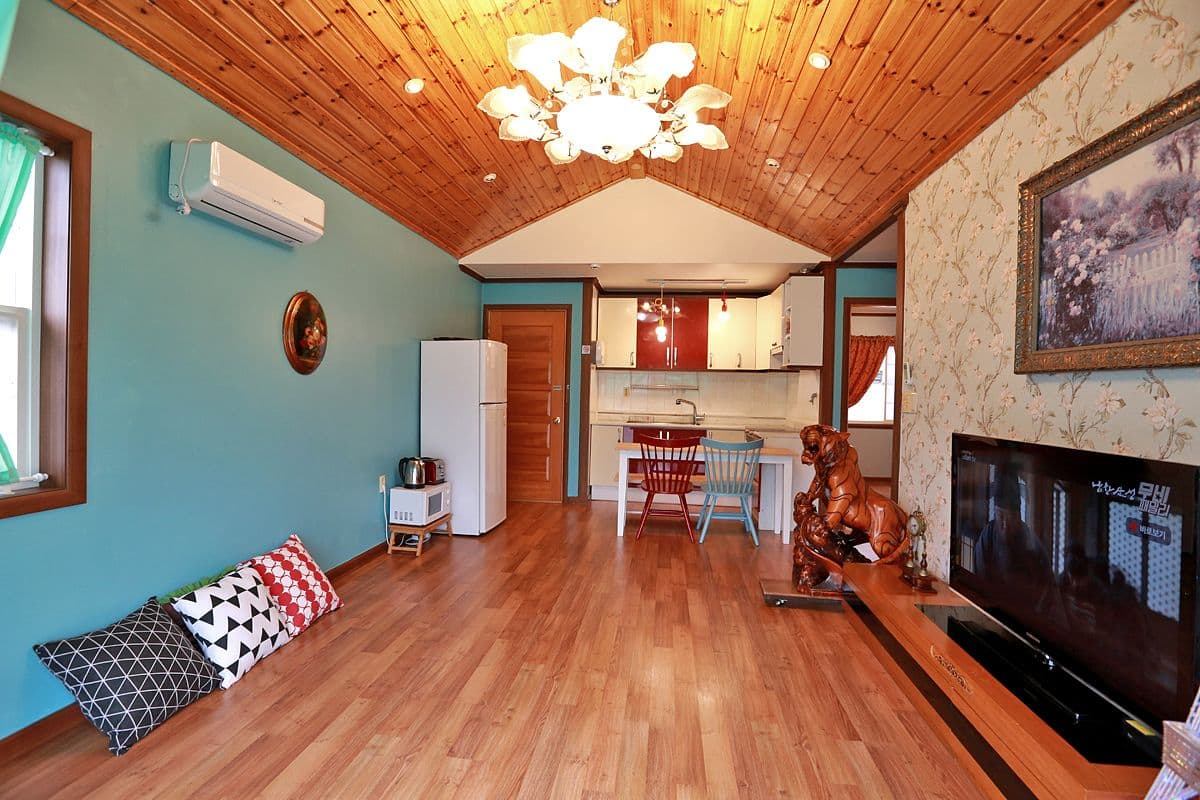 A cozy living room with a wooden ceiling, a TV, a fireplace, and a dining area with chairs and a table.