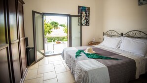 Ein Schlafzimmer mit einem Bett, einem Gemälde, einem Fernseher und einer Glasdoor, die auf einen Balkon führt.