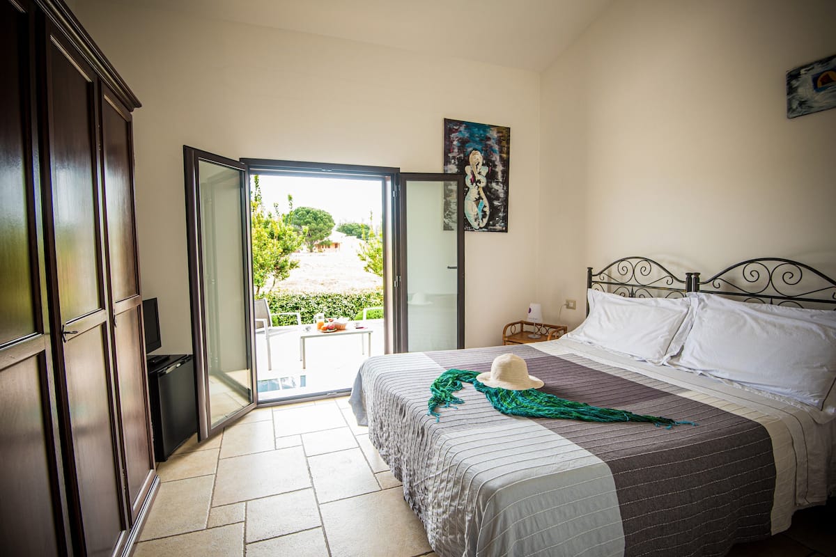 A bedroom with a bed, a painting, a television, and a sliding glass door leading to a balcony.