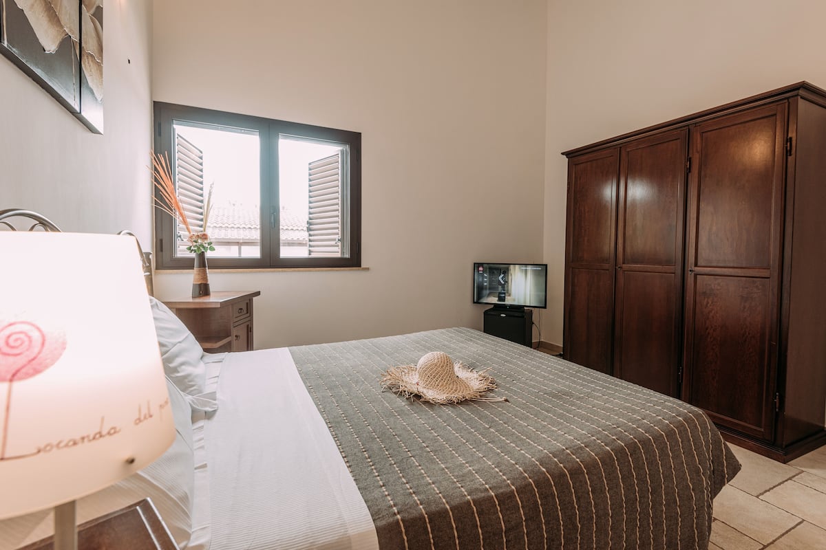 A bedroom with a bed, a nightstand, a lamp, a window, and a wardrobe.