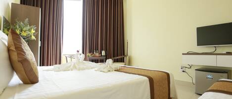 A hotel room with a large bed, a flat-screen TV, a mini-fridge, and a desk with a chair.