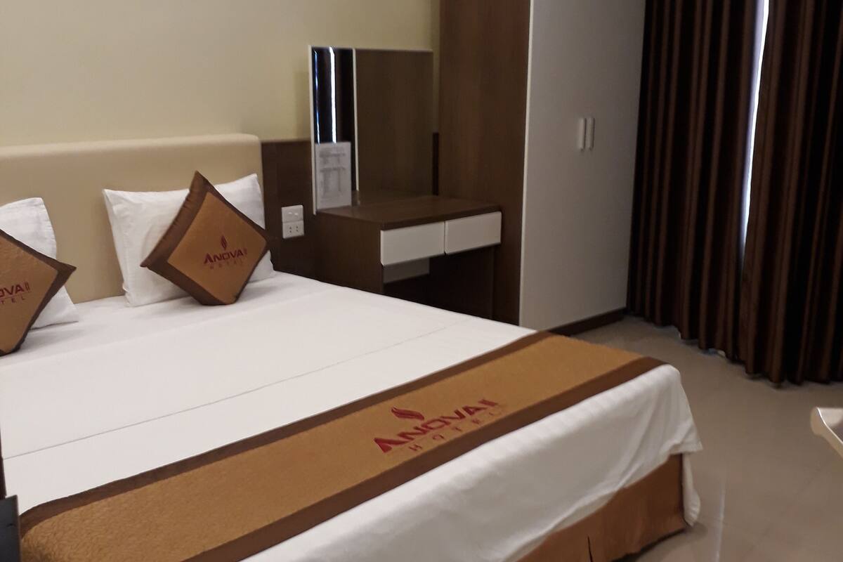 A hotel room with a large bed, a desk, a wardrobe, and a mirror.