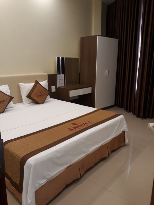 A hotel room with a large bed, a desk, a wardrobe, and a mirror.