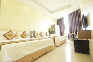 Quarto de hotel com duas camas, uma escrivaninha, uma televisão e uma janela com cortinas.