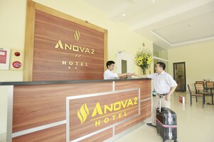 Bancada de recepção no NOVA2 HOTEL, com acabamento em madeira e um logotipo.