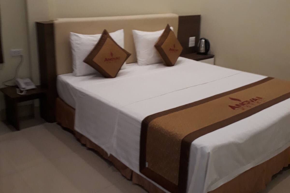 A hotel room with a bed, a nightstand, a telephone, and a wall-mounted light fixture.