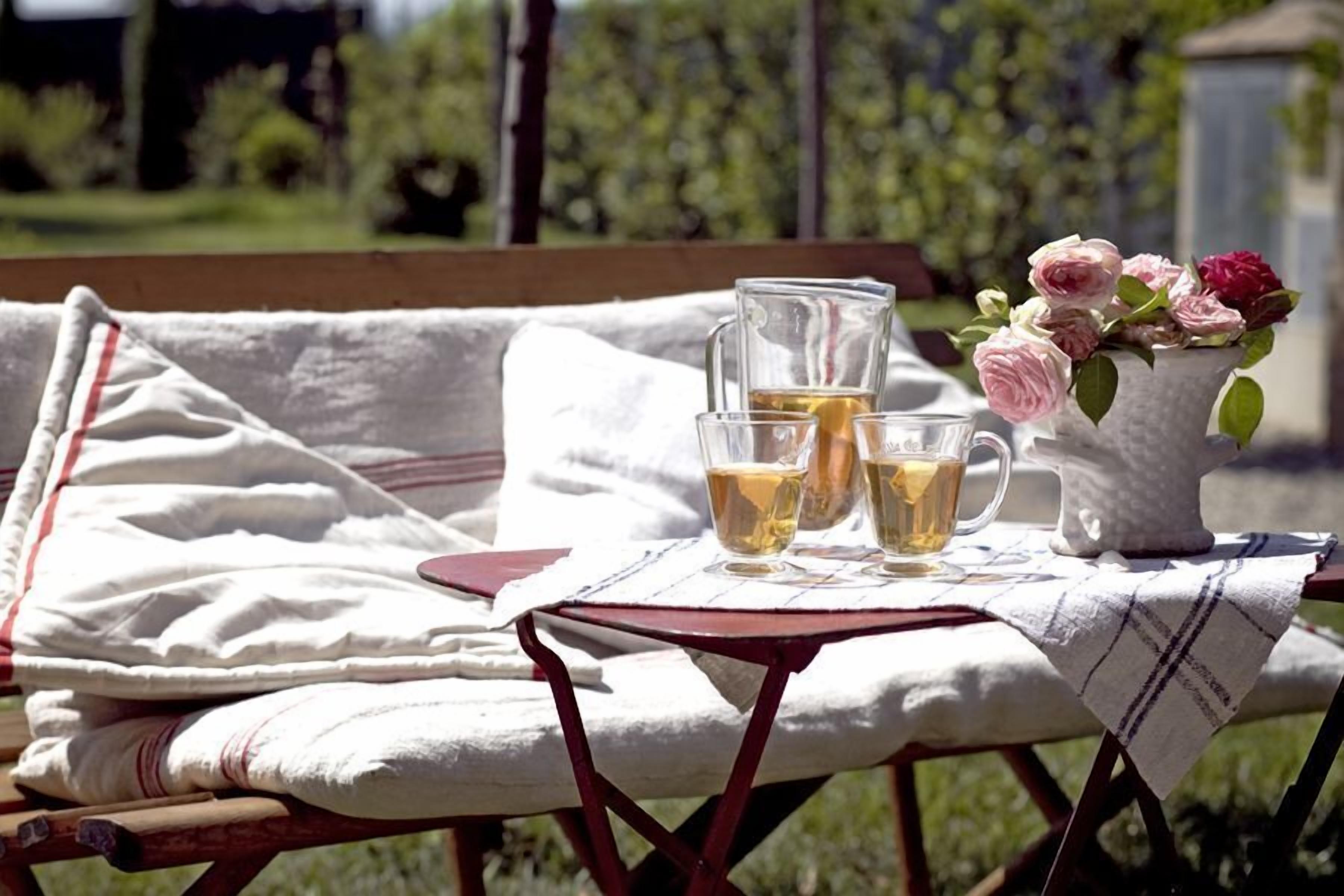 A table with a pitcher, two glasses, and a vase of flowers on a bench outdoors.