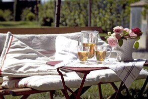 A table with a pitcher, two glasses, and a vase of flowers on a bench outdoors. - Villino Di Porporano (Parma)