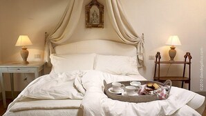 Un lit bien fait, surmonté d’un baldaquin, deux tables de chevet avec des lampes, et un plateau contenant des éléments pour le petit-déjeuner.