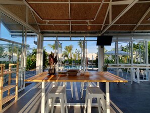 A covered outdoor dining area with a pool view, white stools, and a wooden table. - Meet Boutique Resort (Phunphin)