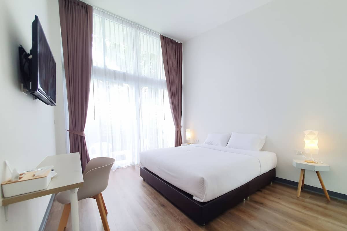 A hotel room with a bed, a desk, a chair, a TV, and two bedside lamps.