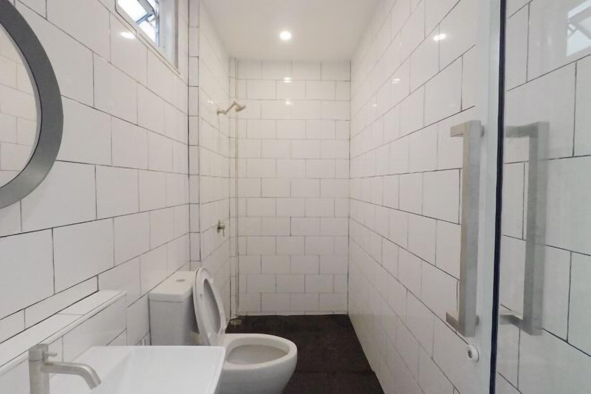 A narrow bathroom with white tiled walls, a toilet, and a glass shower enclosure.