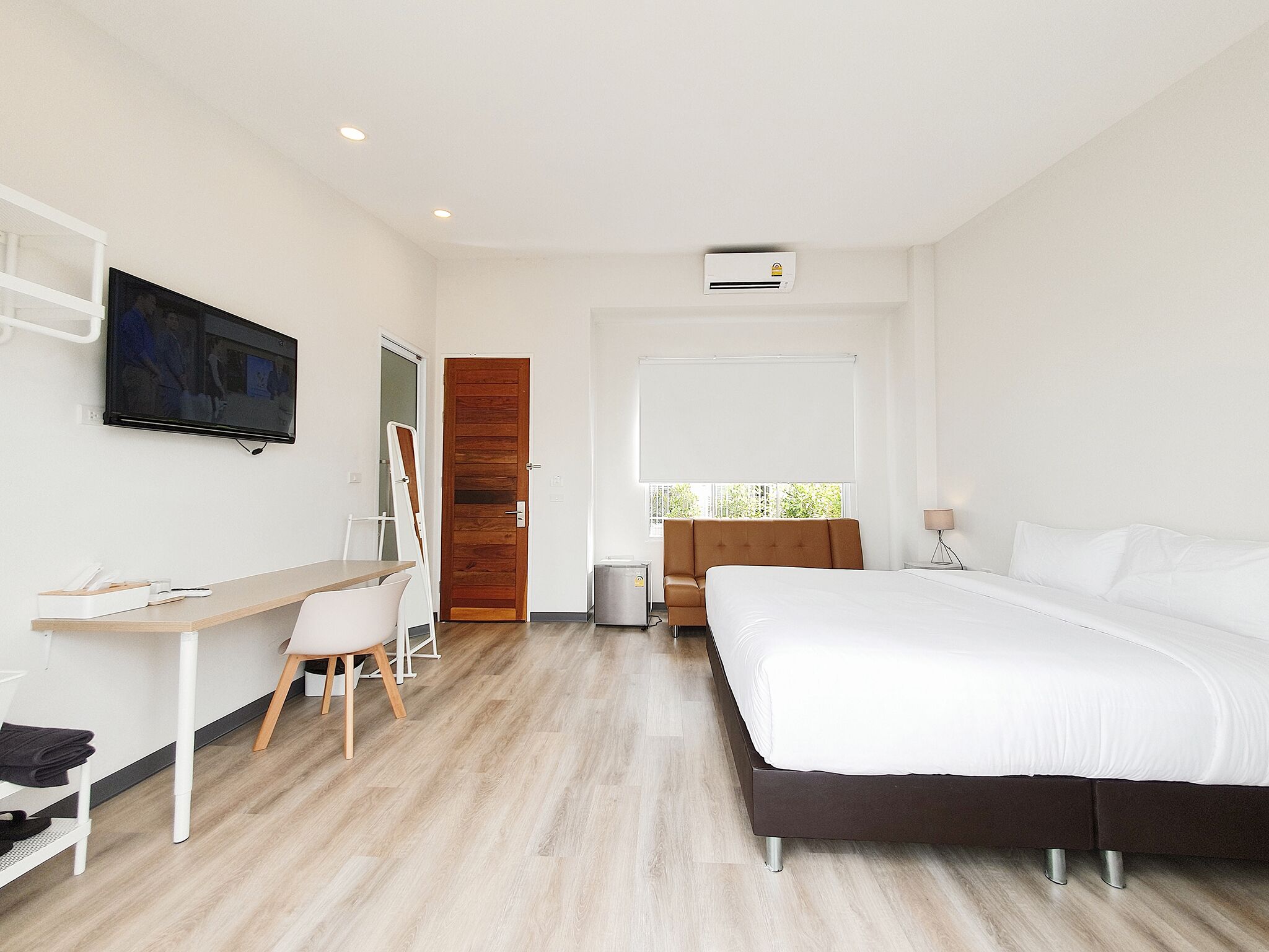 A modern hotel room with a bed, desk, chair, TV, and window.