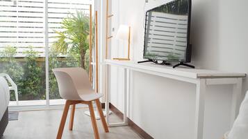 Una habitación moderna con un ventanal grande, un televisor sobre un mueble, una silla blanca y una cama.