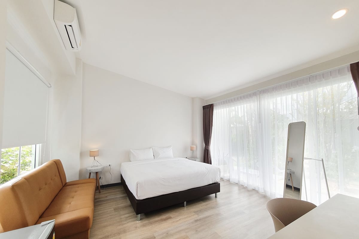 A hotel room with a bed, a sofa, a desk, a chair, and a large window with curtains.