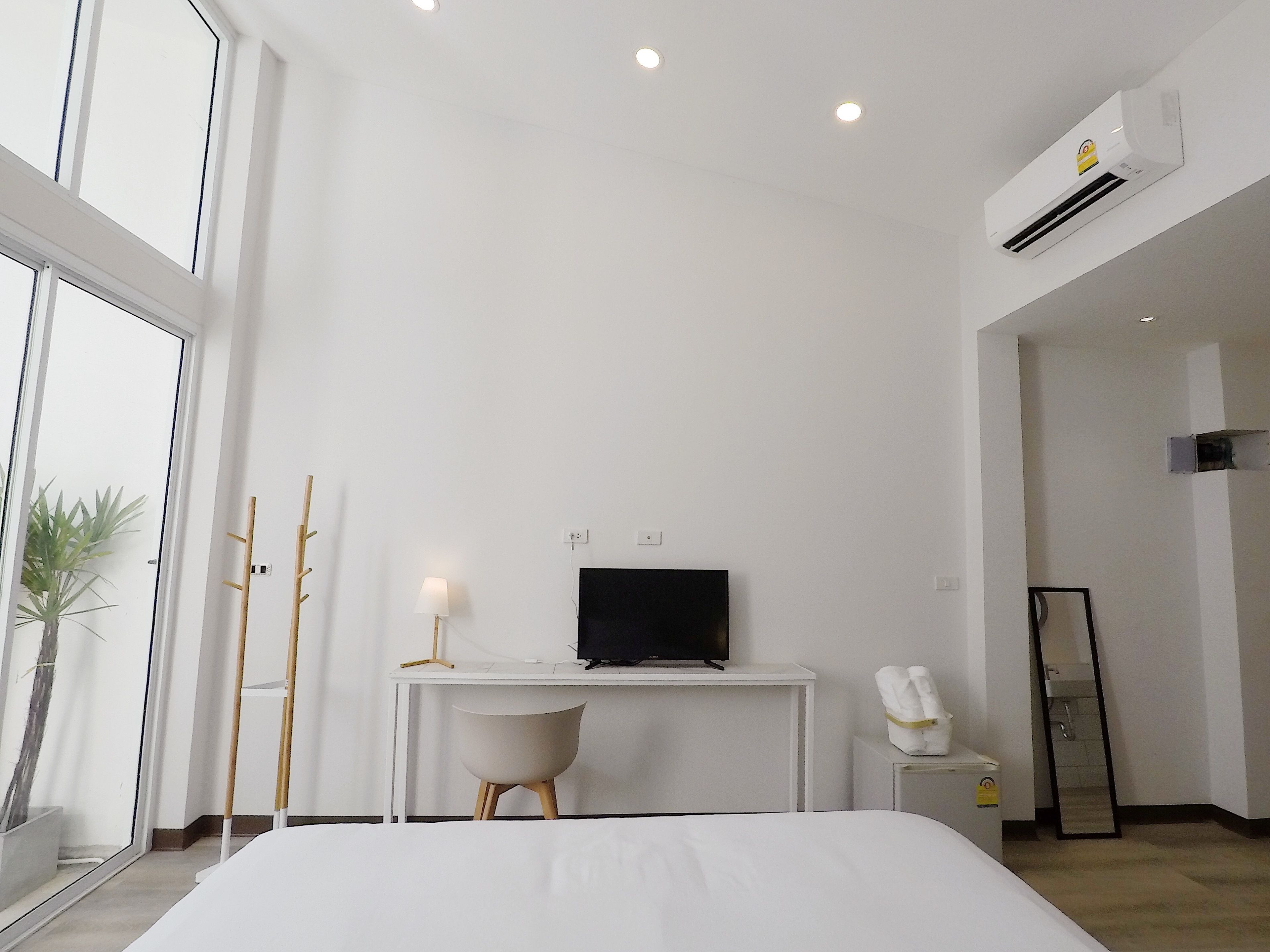 A modern hotel room with a large bed, a desk with a TV, a bedside table with a lamp, and a bathroom visible through an open door.