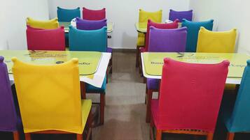 Un espace repas avec des tables et des chaises, chacune agrémentée d’un set de table jaune et du logo de Canary Hotel Partners.