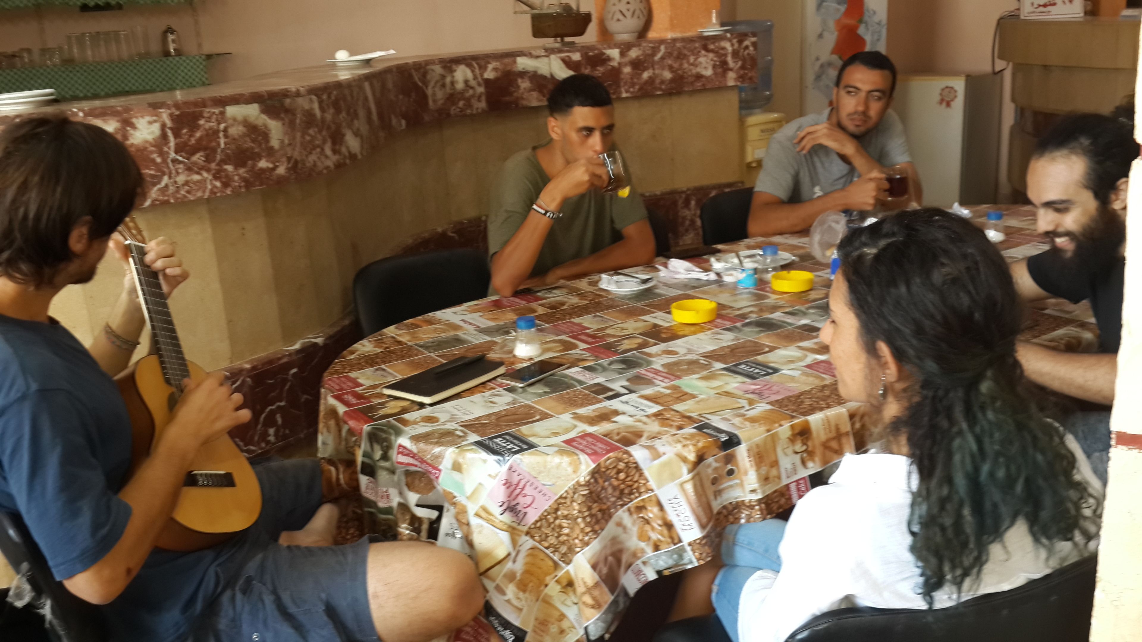 Un gruppo di persone sedute attorno a un tavolo con una tovaglia decorata, impegnate in una conversazione.