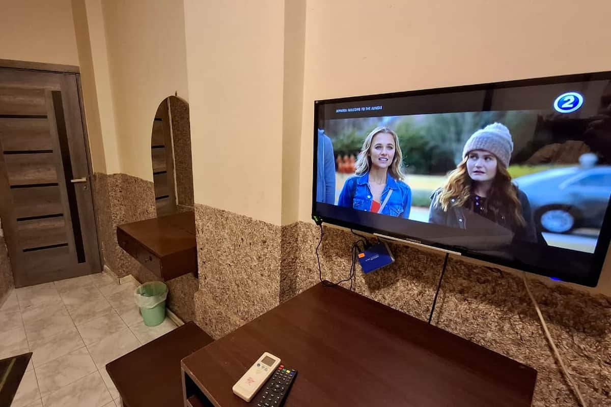 A living room with a flat-screen TV mounted on the wall, a wooden coffee table, and a remote control on the table.