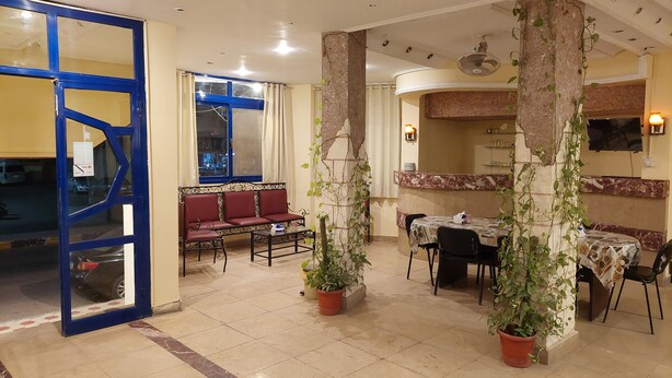 A dining area with a blue-framed entrance, a sofa, a table with chairs, and potted plants.