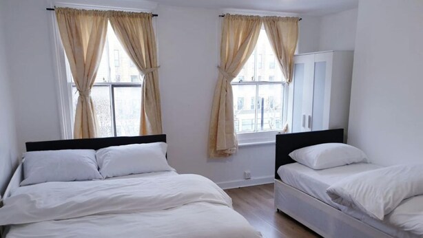 Quarto com duas camas, um guarda-roupa e uma janela com cortinas.