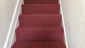 Uma escadaria com degraus revestidos de carpete vermelho e corrimãos brancos.