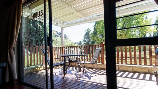 A covered patio with a table and chairs, a wooden deck, and a view of a mountainous landscape. - La Bri Self Catering (Clarens)